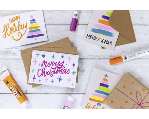 Cartes de Noël avec des motifs et des couleurs de Noël, entourées de matériel de bricolage comme des stylos et des peintures