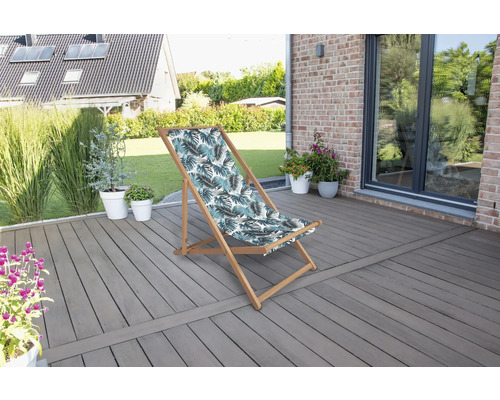 Scène de jardin avec une chaise longue à motif de feuilles sur une terrasse.