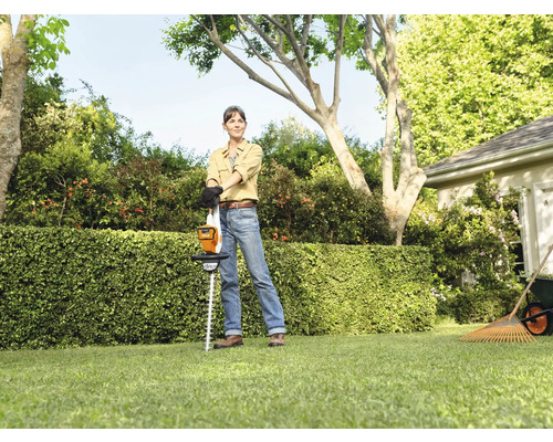 Femme avec un taille-haie à batterie dans le jardin devant une haie.