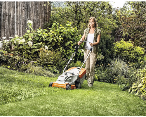 Frau bedient Rasenmäher im Garten.