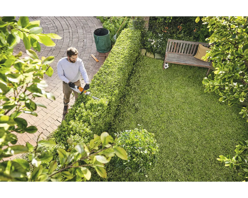 Ein Mann schneidet eine Hecke mit einer Heckenschere in einem Garten.