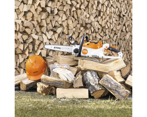 Tronçonneuse à batterie avec casque de protection, lunettes de protection et gants sur une pile de bois