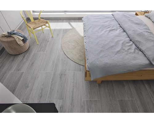 Chambre avec lit, chaise, tabouret, tapis et carrelage de sol gris aspect bois