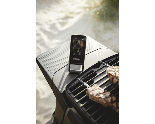 Enders Logo auf einem Grillthermometer neben einem Grill mit Fleisch.