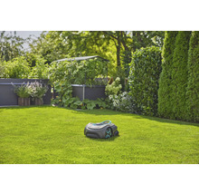 Robot tondeuse à gazon sur pelouse devant un jardin avec plates-bandes surélevées et haies
