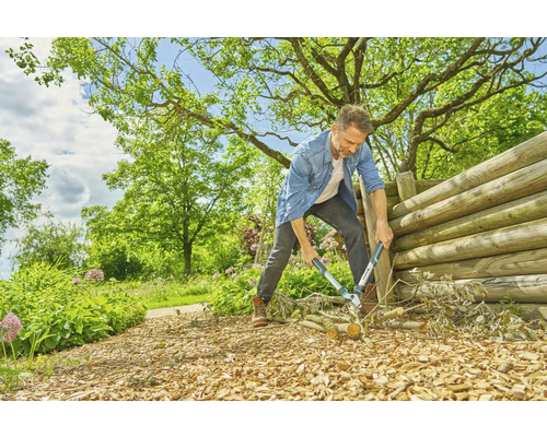 Un homme coupe des branches avec un sécateur dans un jardin avec une clôture en bois.
