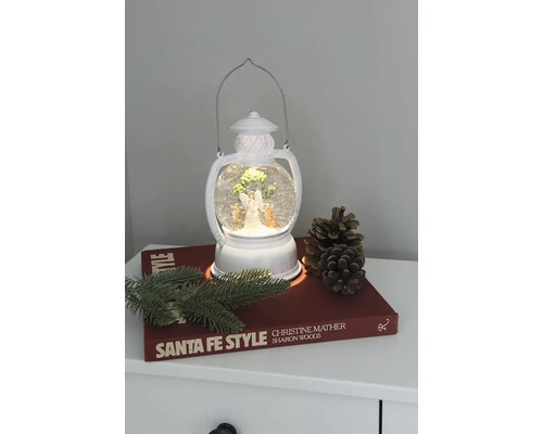 Dekorative Laterne mit Schneekugel, Engel und Tannenbaum auf einem Nachttisch