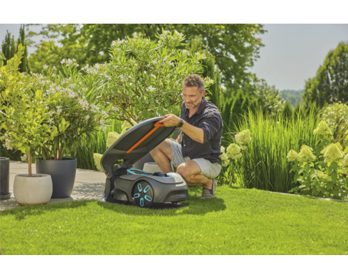 Un homme ouvre le couvercle d''un robot tondeuse à gazon sur une pelouse