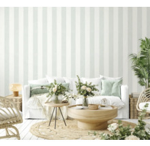 Salon lumineux avec papier peint rayé, canapé, table et plantes pour une atmosphère conviviale.