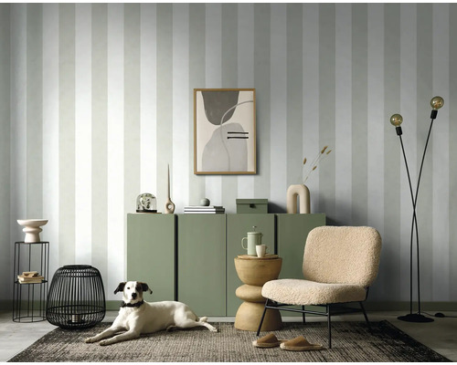 Salon avec papier peint rayé, commode, fauteuil, lampadaire et chien