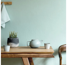 Holztisch mit Teekanne, Tassen und Pflanze im Topf vor einer Wand