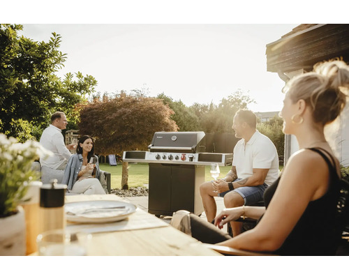 Des personnes sont assises dans le jardin avec un barbecue à gaz.