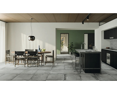 Salon lumineux avec coin repas, îlot de cuisine et carrelage gris.