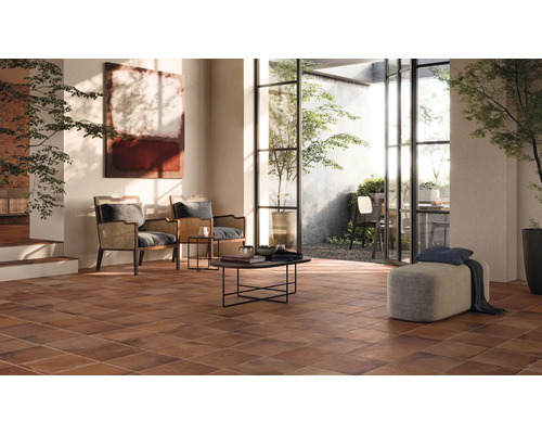 Wohnzimmer mit braunen Bodenfliesen, Sitzgelegenheiten und Zugang zum Aussenbereich.