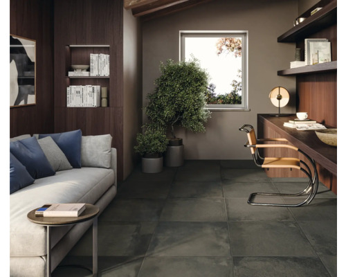 Wohnzimmer mit Sofa, Schreibtisch und dunklen Bodenfliesen.