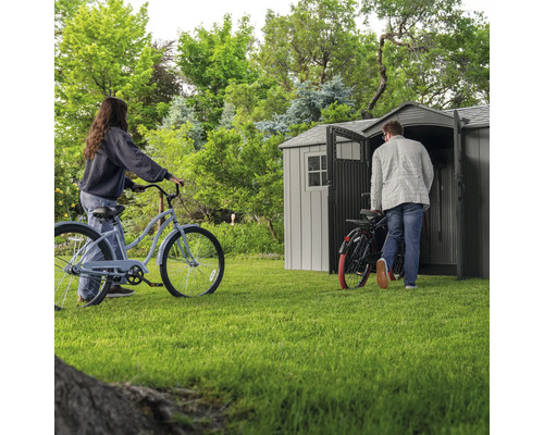 Scène de jardin avec abri de jardin et deux personnes avec des vélos sur une pelouse