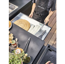 Une personne ouvre un tiroir contenant des accessoires de barbecue dans une cuisine extérieure.