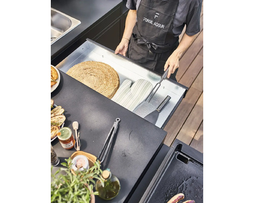 Une personne ouvre un tiroir contenant des accessoires de barbecue dans une cuisine extérieure.