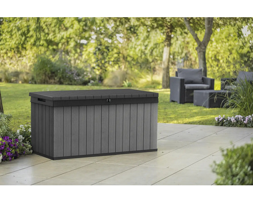 Graue Gartenbox aus Kunststoff auf einer Terrasse mit Gartenmöbeln im Hintergrund