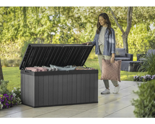 Geöffnete Gartenbox aus Kunststoff mit Kissen und einer Frau im Garten