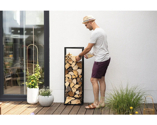 Mann befüllt Brennholzregal mit Holz auf einer Terrasse