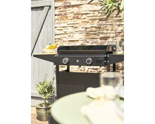 Aussenaufnahme einer schwarzen Plancha-Grillstation auf einer Terrasse, mit Mauerwerk im Hintergrund