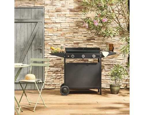 Extérieur avec chariot de grill, table de jardin et chaises devant un mur en pierre