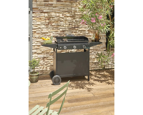 Photo d''extérieur d''un barbecue à gaz noir à trois brûleurs sur une terrasse en bois avec un mur de pierre en arrière-plan.