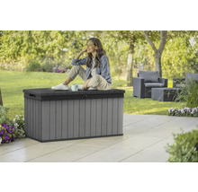 Szene im Garten mit grauer Aufbewahrungsbox aus Kunststoff, auf der eine Frau sitzt