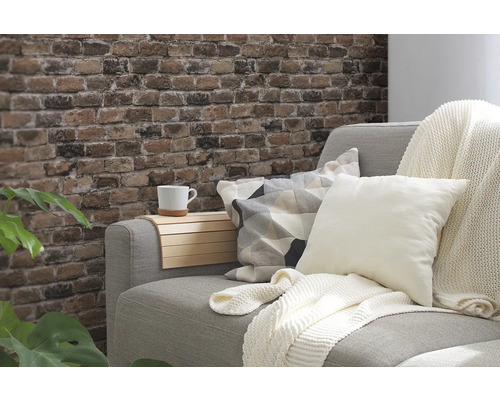 Dekoratives Wohnzimmer mit grauer Couch, Kissen, Überwurf und Wand in Backsteinoptik.