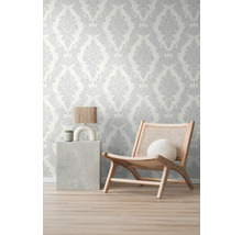 Raumansicht mit gemusterter Tapete, einem Sessel und einem Beistelltisch mit Lampe und Pflanze