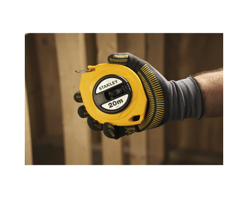 Une main gantée tient un mètre ruban jaune Stanley de 20 mètres.