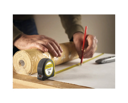 Une personne mesure un rouleau de papier peint avec un mètre ruban et le marque avec un crayon.