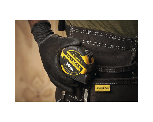 Une personne tient un mètre à ruban Stanley Fatmax de 10 mètres.