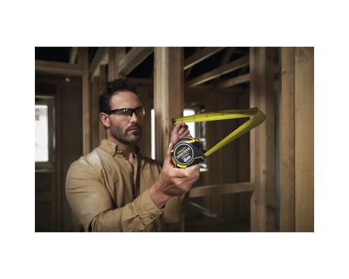 Ein Mann misst mit einem gelben Stanley Fatmax Rollbandmass von 8 Metern in einem Rohbau.