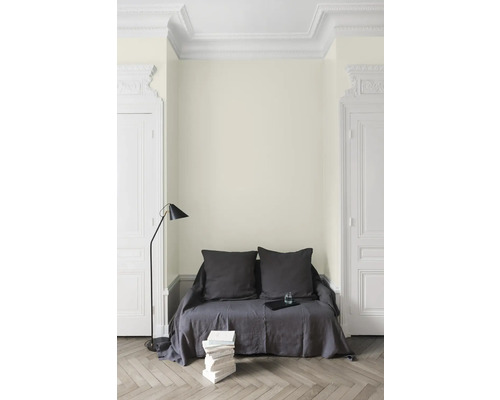 Wohnraum mit hellem Wandanstrich, Sofa mit Kissen, Stehlampe und Bücherstapel