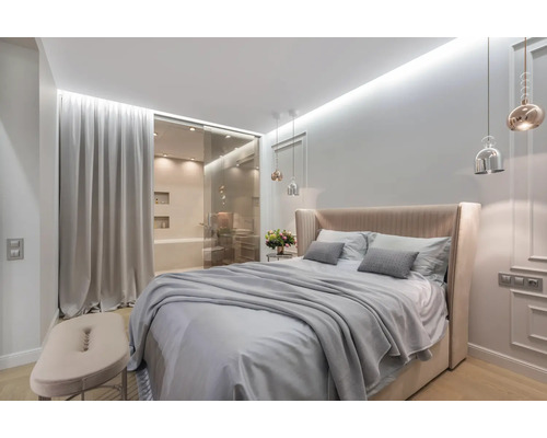 Helles Schlafzimmer mit Doppelbett, Nachttisch und angrenzendem Badezimmer hinter einer Glasschiebetür