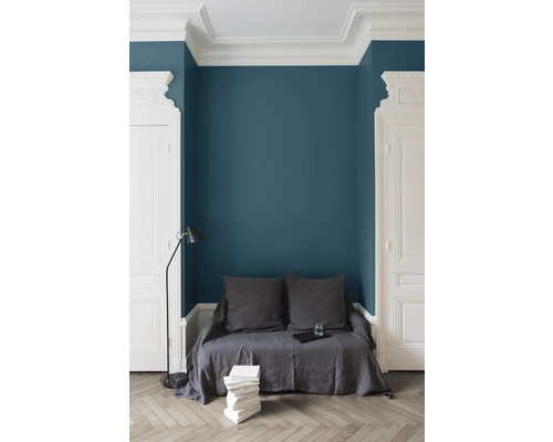Heller Raum mit blauer Wand, Stuckdekor, Sitzgelegenheit mit Kissen, Bücherstapel und Stehleuchte