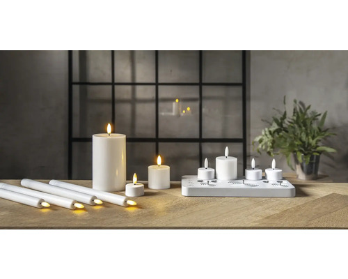 Bougies LED décoratives sur une table en bois devant une fenêtre.