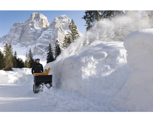 Mann benutzt eine Schneefräse zum Schneeräumen vor einer Bergkulisse.