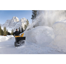 Un homme utilise une souffleuse à neige pour déneiger devant un paysage de montagne