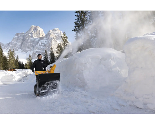Mann benutzt Schneefräse zum Schneeräumen vor Bergkulisse