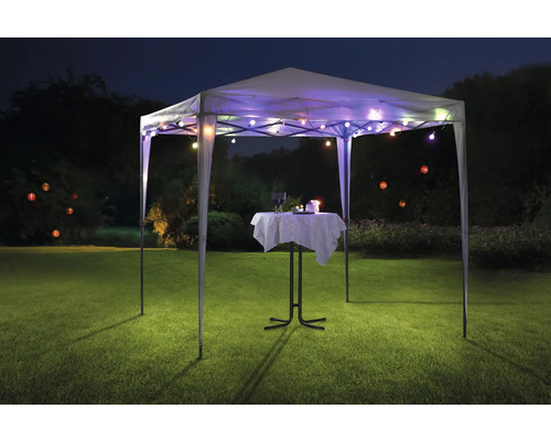 Tente de réception avec guirlande lumineuse et table de bistro sur une pelouse