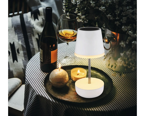 Dekoratives Ambiente mit Tischleuchte, Kerzen, Wein und Blumenvase auf einem Tisch.