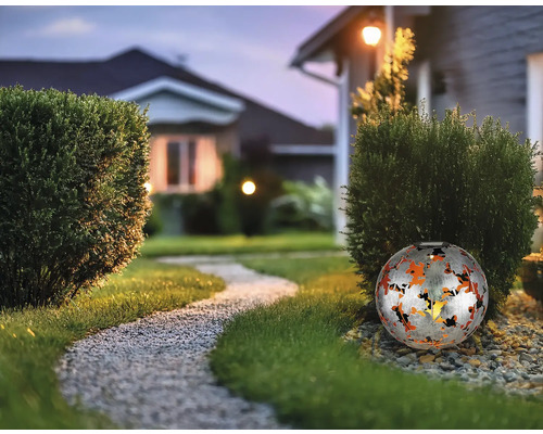 Dekorative Gartenleuchte in Kugelform aus Metall mit Muster entlang eines Gartenwegs