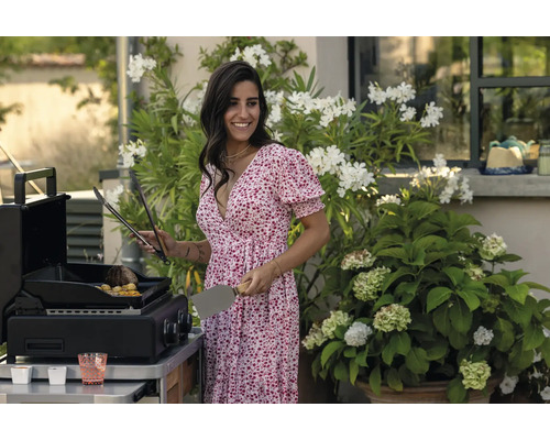 Femme faisant des grillades sur une cuisine extérieure avec une pince à barbecue et une spatule