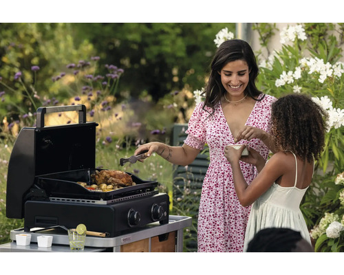 Une femme et un enfant font des grillades dans le jardin avec un barbecue à gaz. Un poulet rôti est posé sur le gril.