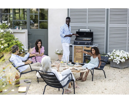 Groupe de personnes assises sur des chaises à l''extérieur avec un maître de grill au fond