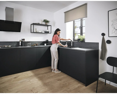 Cuisine moderne avec armoires noires, évier et robinet, hotte aspirante, étagère et une femme remplissant un verre d''eau.