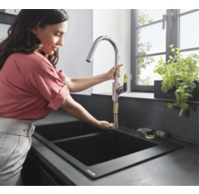 Femme installant un robinet de cuisine chromé dans un évier noir.